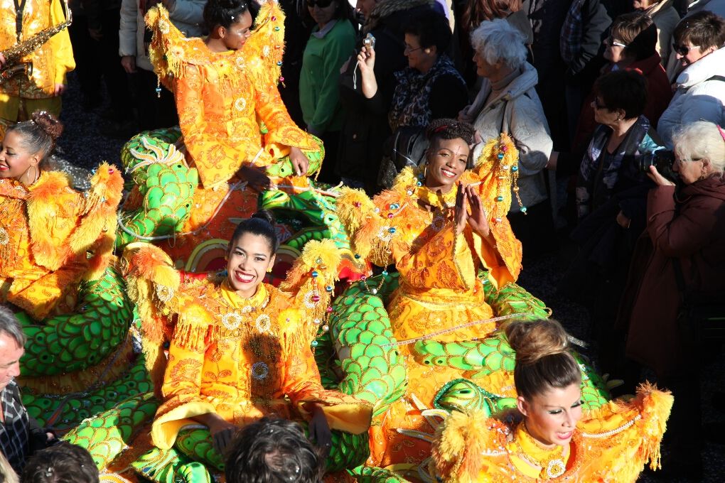 Bunte Karnevalsteilnehmerinnen in prächtigen Kostümen umgeben von einer jubelnden Menschenmenge.
