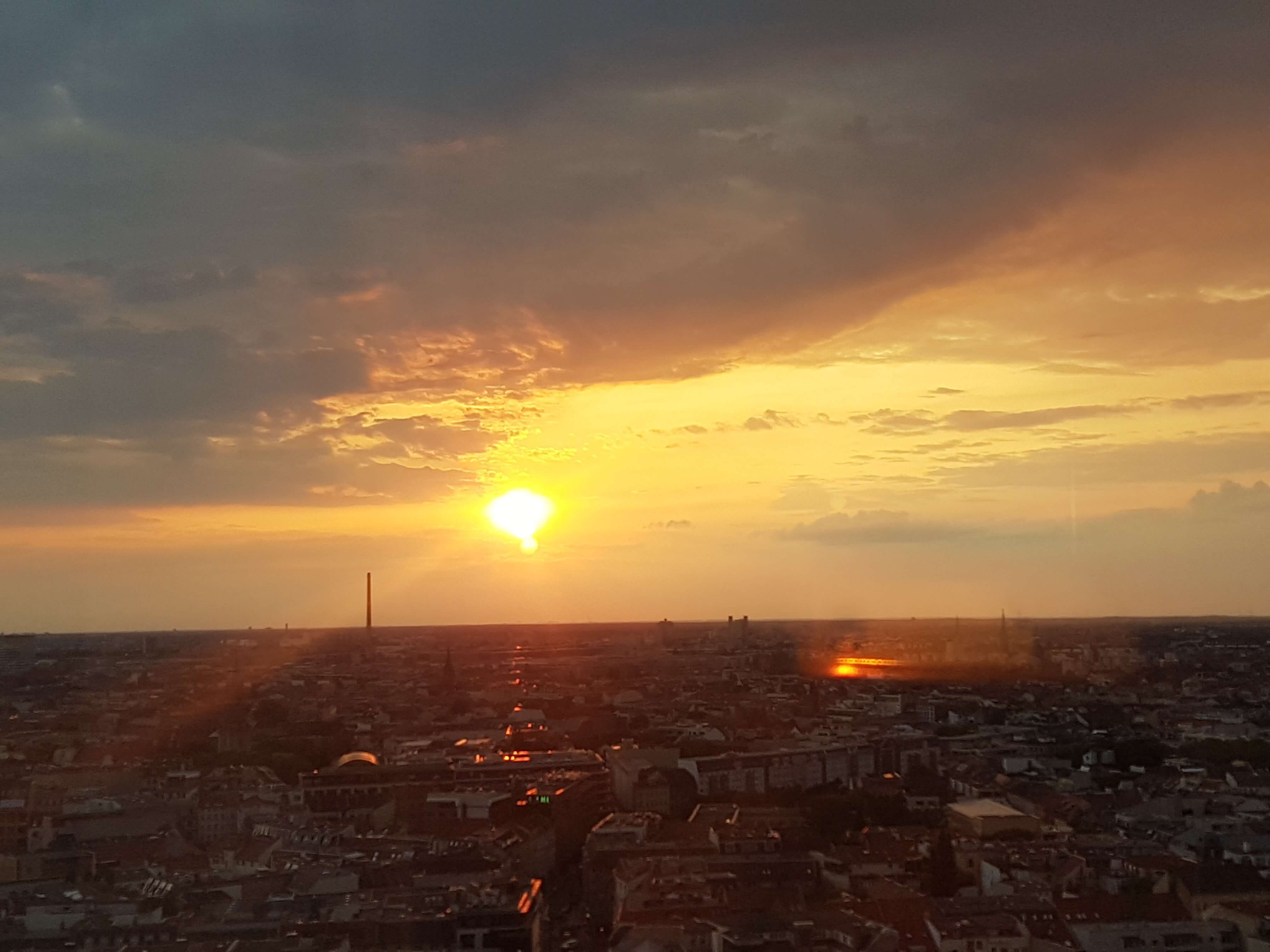 Ein malerischer Sonnenuntergang über einer Stadt, mit orangefarbenen Wolken und der Silhouette von Gebäuden.