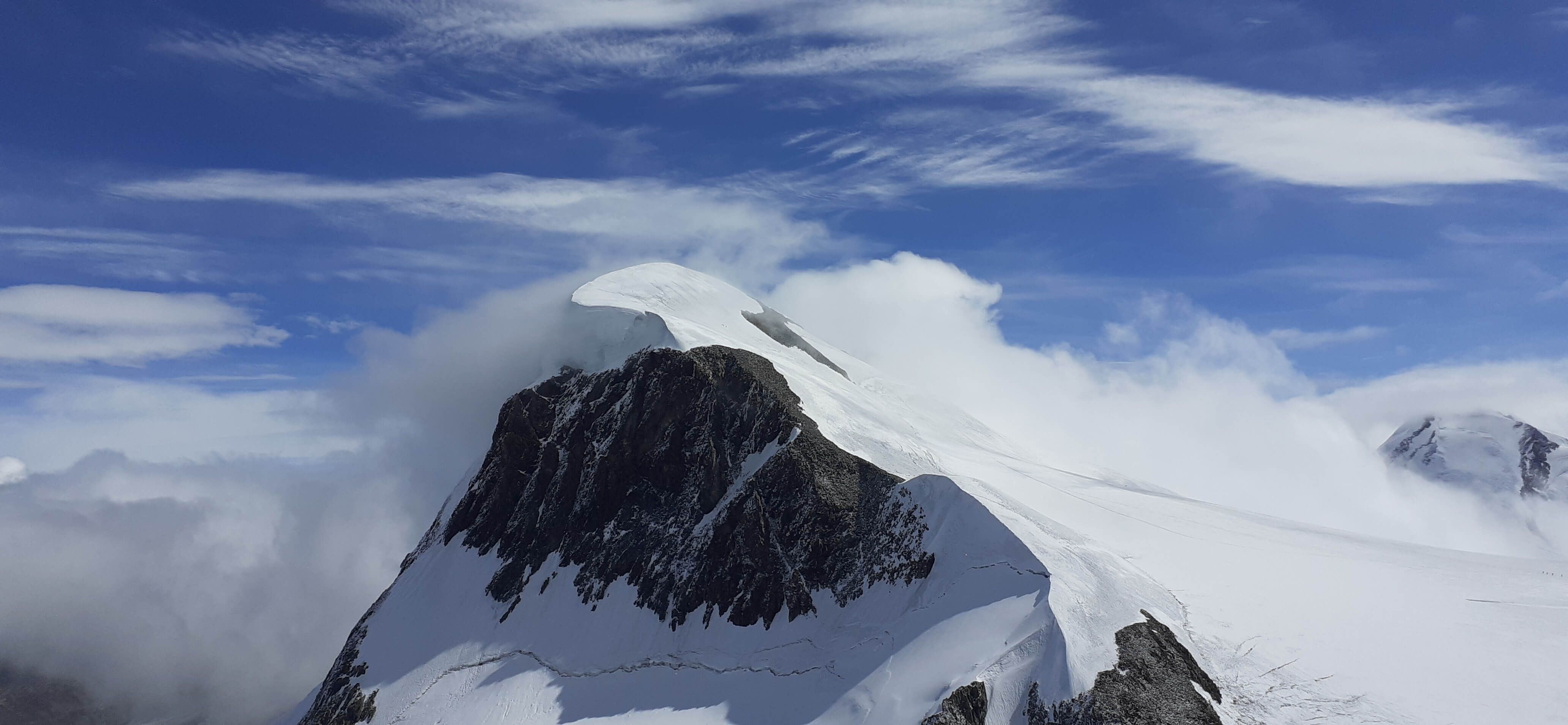 Majestätischer Berg mit schneebedecktem Gipfel, umgeben von Wolken und blauem Himmel. Ein wahres Naturwunder!