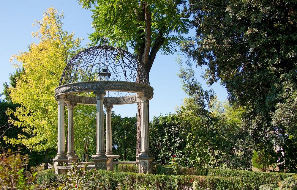 Ein elegantes Gartenpavillon mit kunstvollem Dach, umgeben von bunten Bäumen und dichtem Grün.