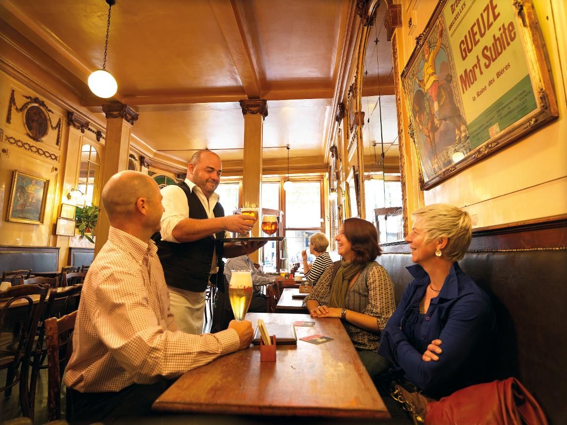 Ein Kellner serviert Getränke an Gäste in einem gemütlichen Restaurant mit warmem Licht und rustikalem Ambiente.