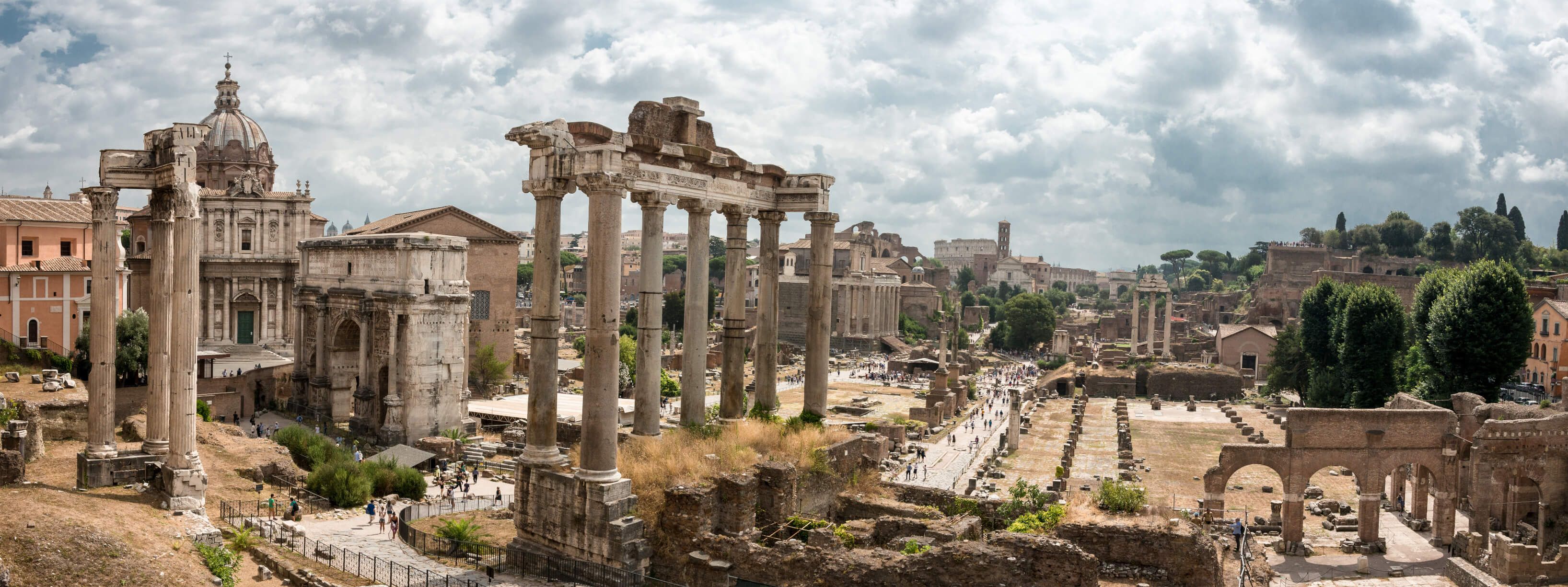 Antike Ruinen in Rom mit Säulen, Tempeln und einer beeindruckenden Architektur unter bewölktem Himmel.