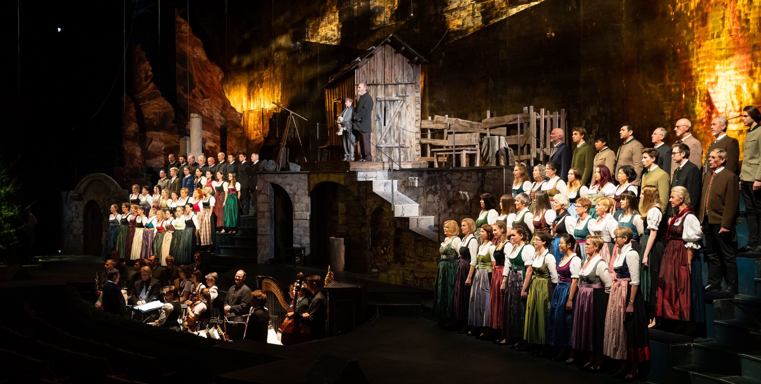 Eine Aufführung mit vielen Sängern in traditioneller Kleidung auf einer Bühnenlandschaft.