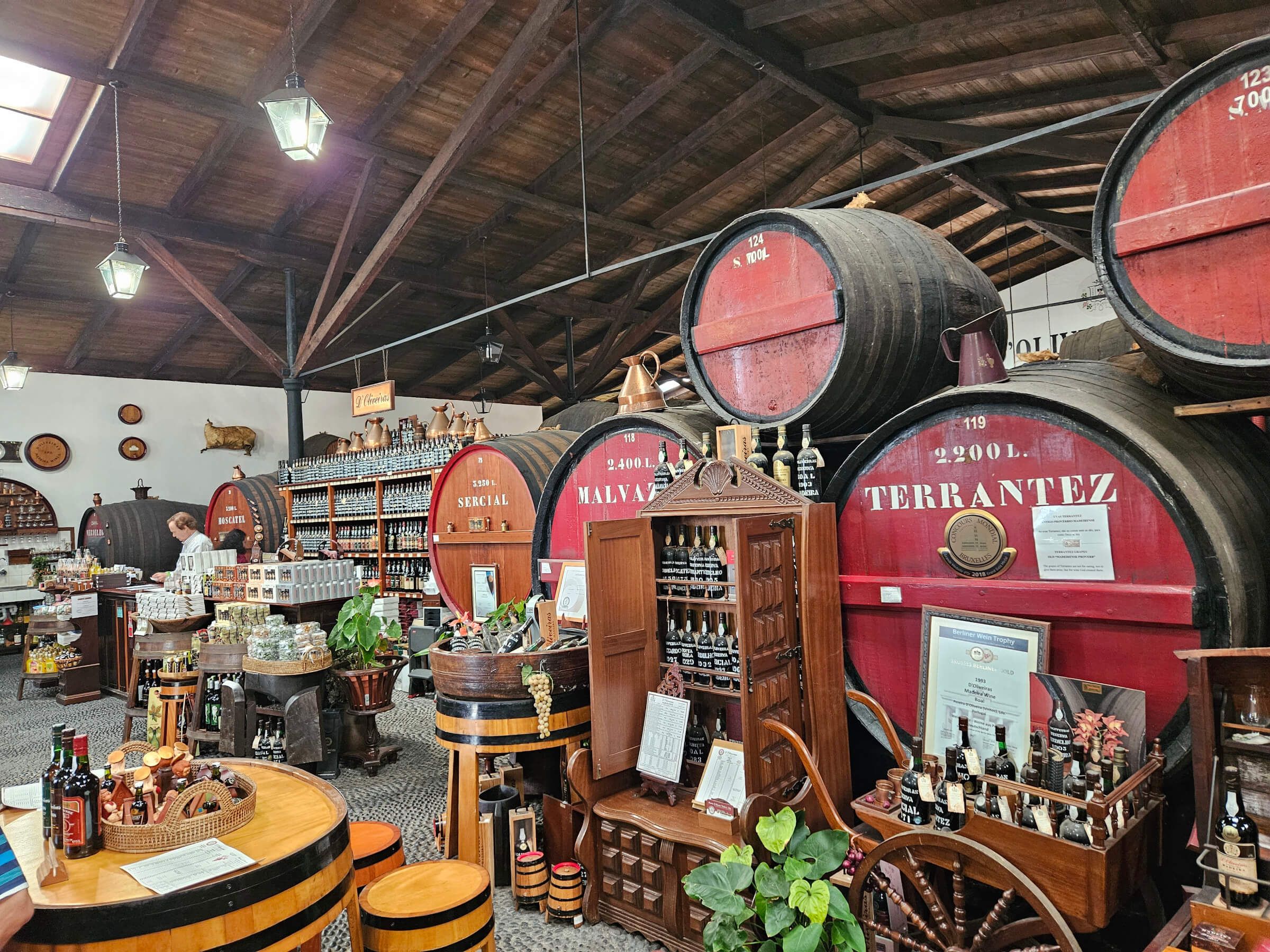 Ein gemütlicher Verkaufsraum mit großen Weinfässern, Regalen mit Flaschen und rustikalen Möbeln.
