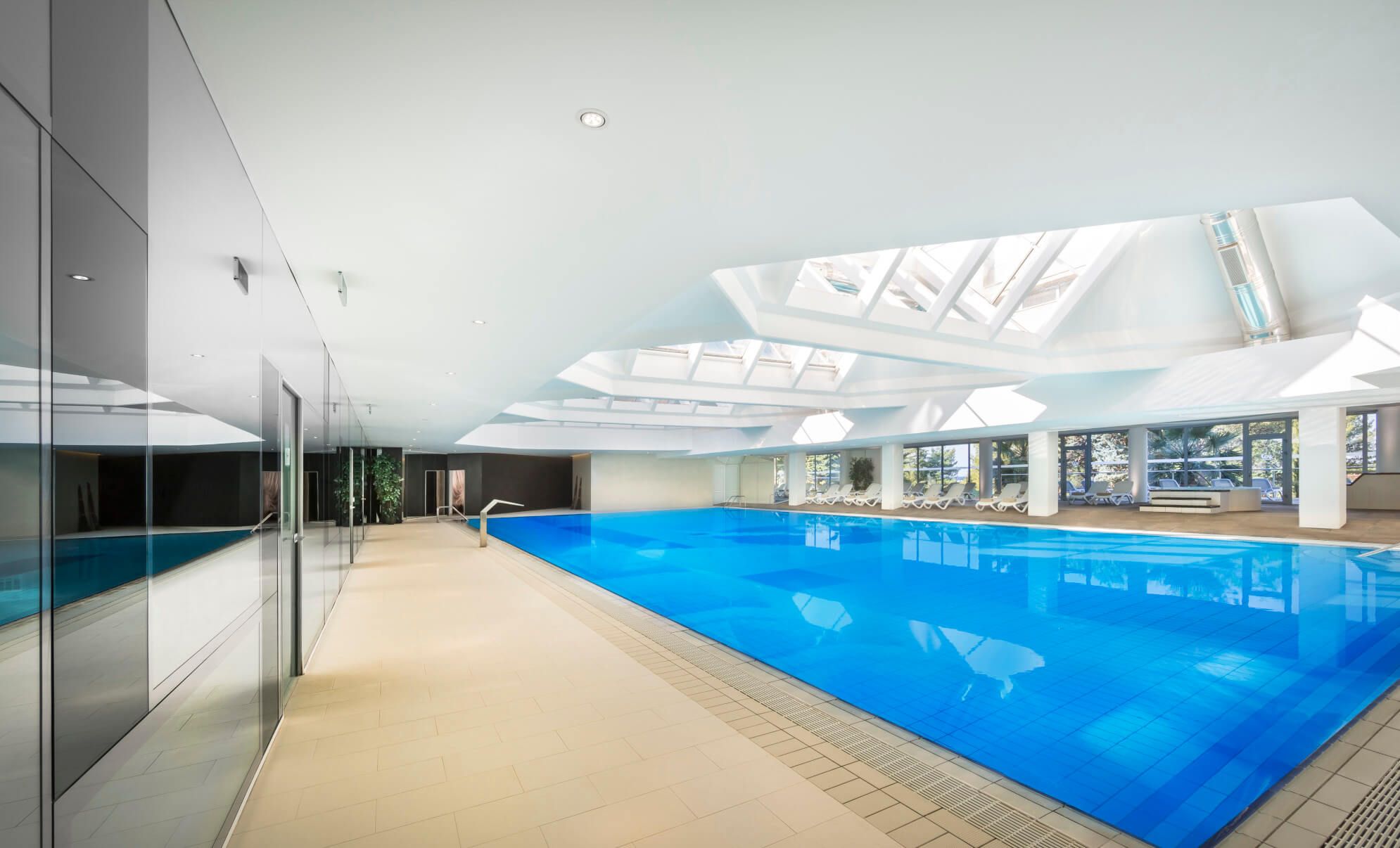 Ein elegantes Hallenbad mit klarem, blauem Wasser und viel natürlichem Licht durch große Fenster und Oberlichter.