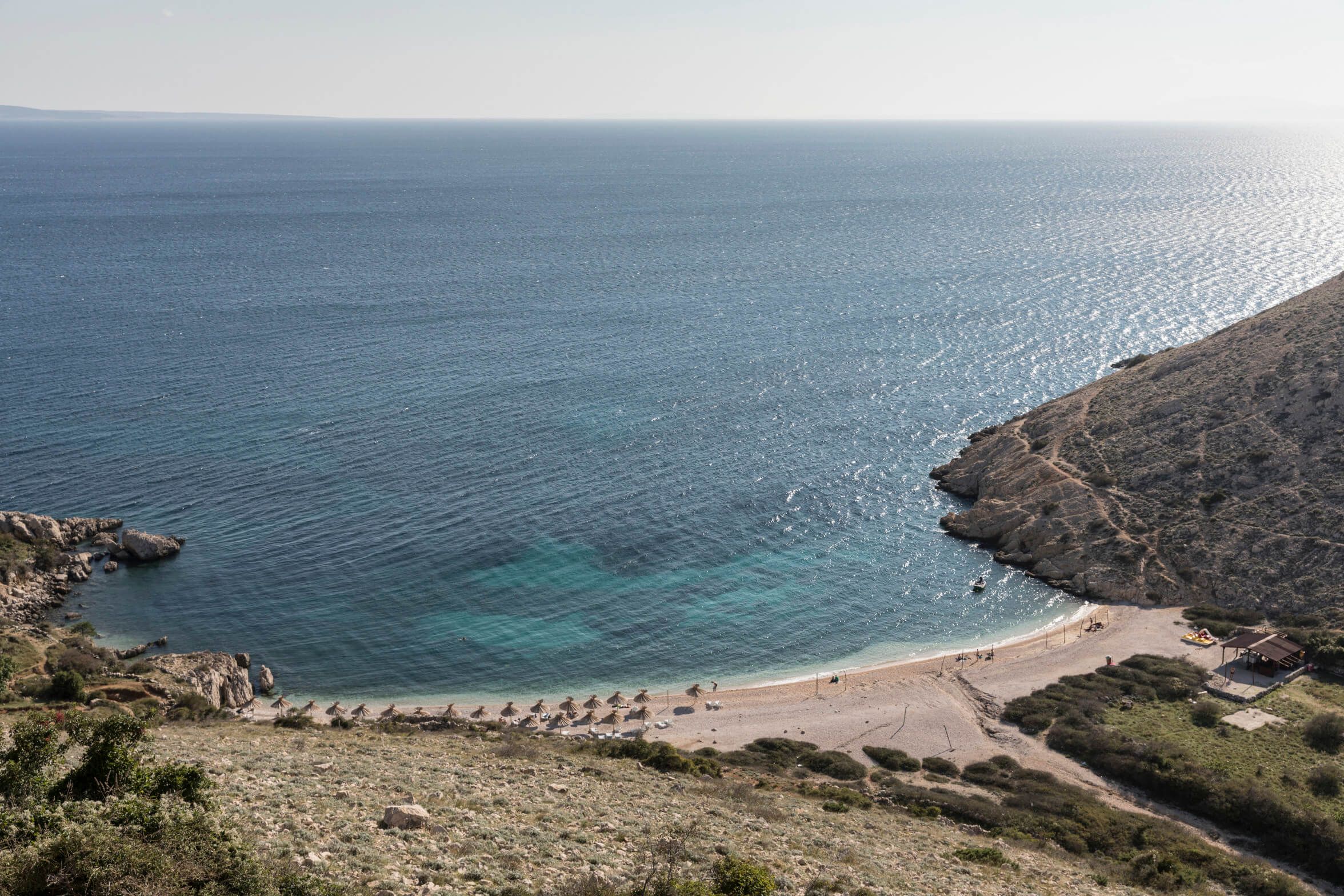 Eine ruhige Küste mit klarem Wasser, sandigem Strand und sanften Hügeln im Hintergrund. Traumhafte Landschaftsaufnahme.