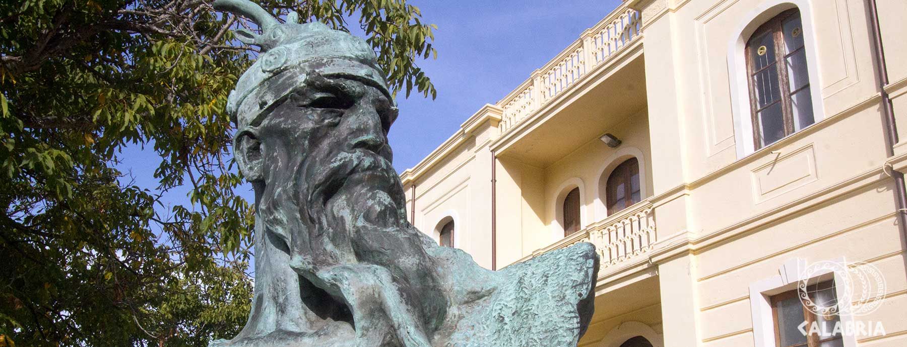 Eine Statue mit detaillierten Gesichtszügen und Kopfputz, im Hintergrund ein Gebäude mit Fenster.