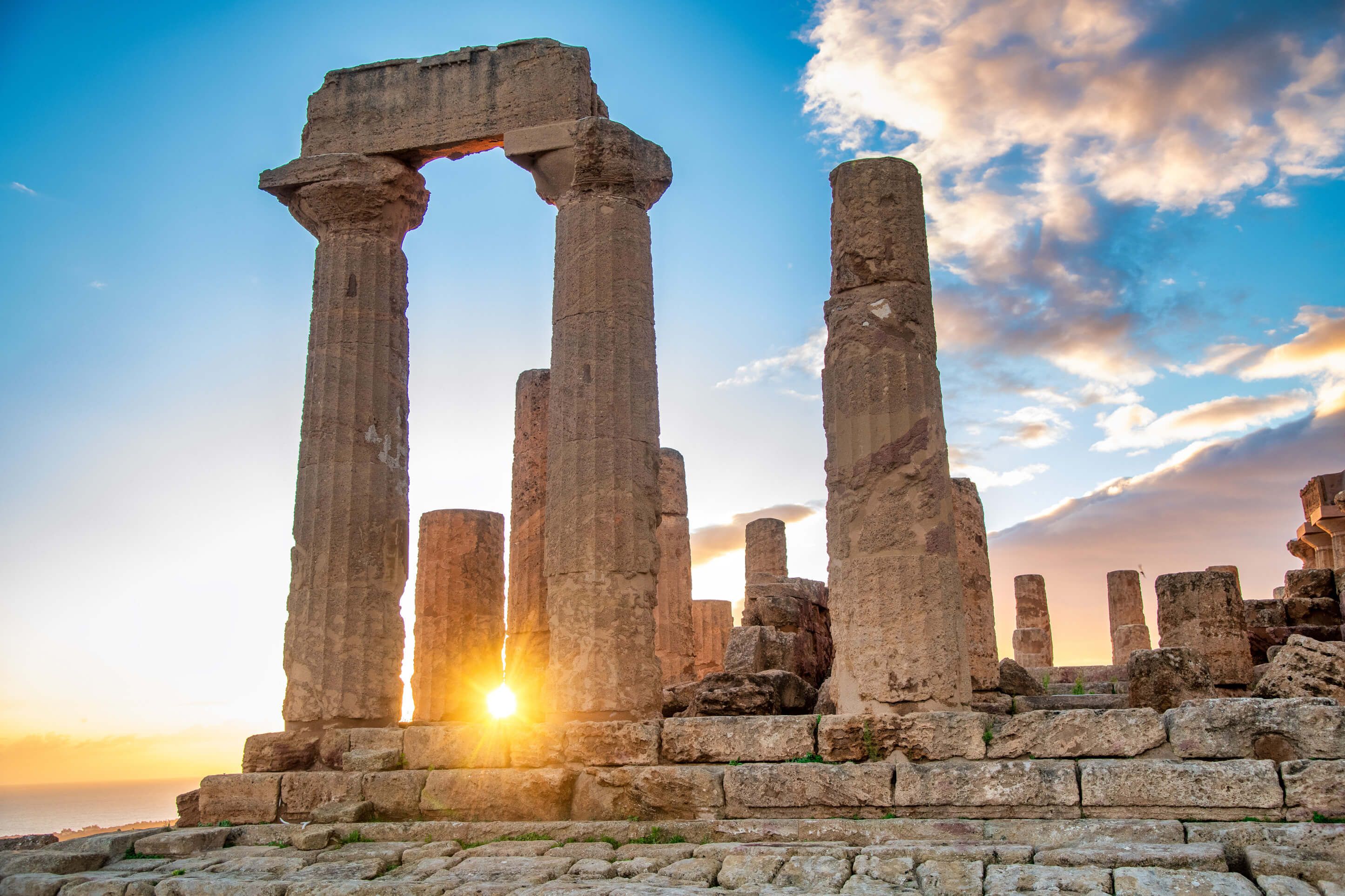 Antike Säulenruinen im Sonnenuntergang, der Himmel leuchtet in sanften Farben über dem Meer.