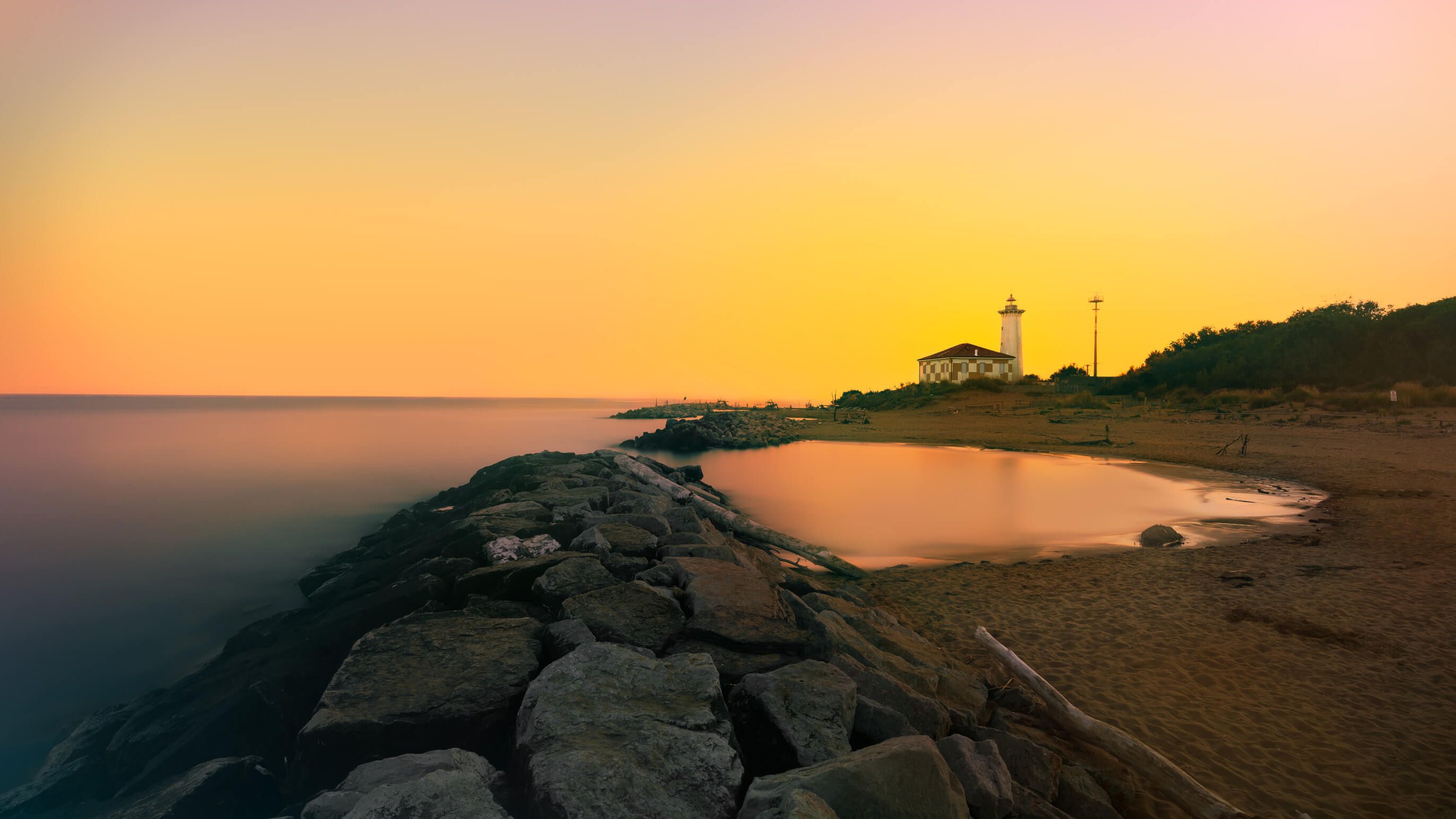 Ein schöner Sonnenuntergang über einem Strand mit Felsen, einem Leuchtturm und ruhigem Wasser.