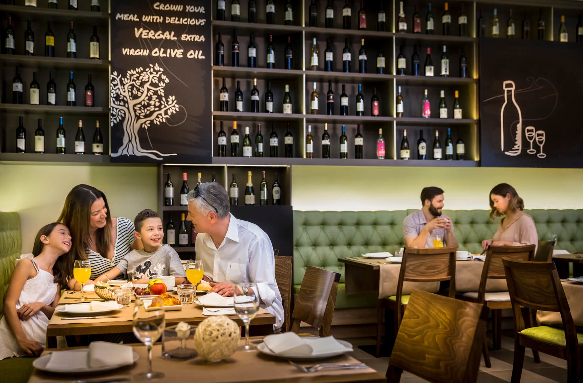 Eine Familie genießt ein Essen in einem modernen Restaurant mit Weinregalen und fröhlicher Atmosphäre.