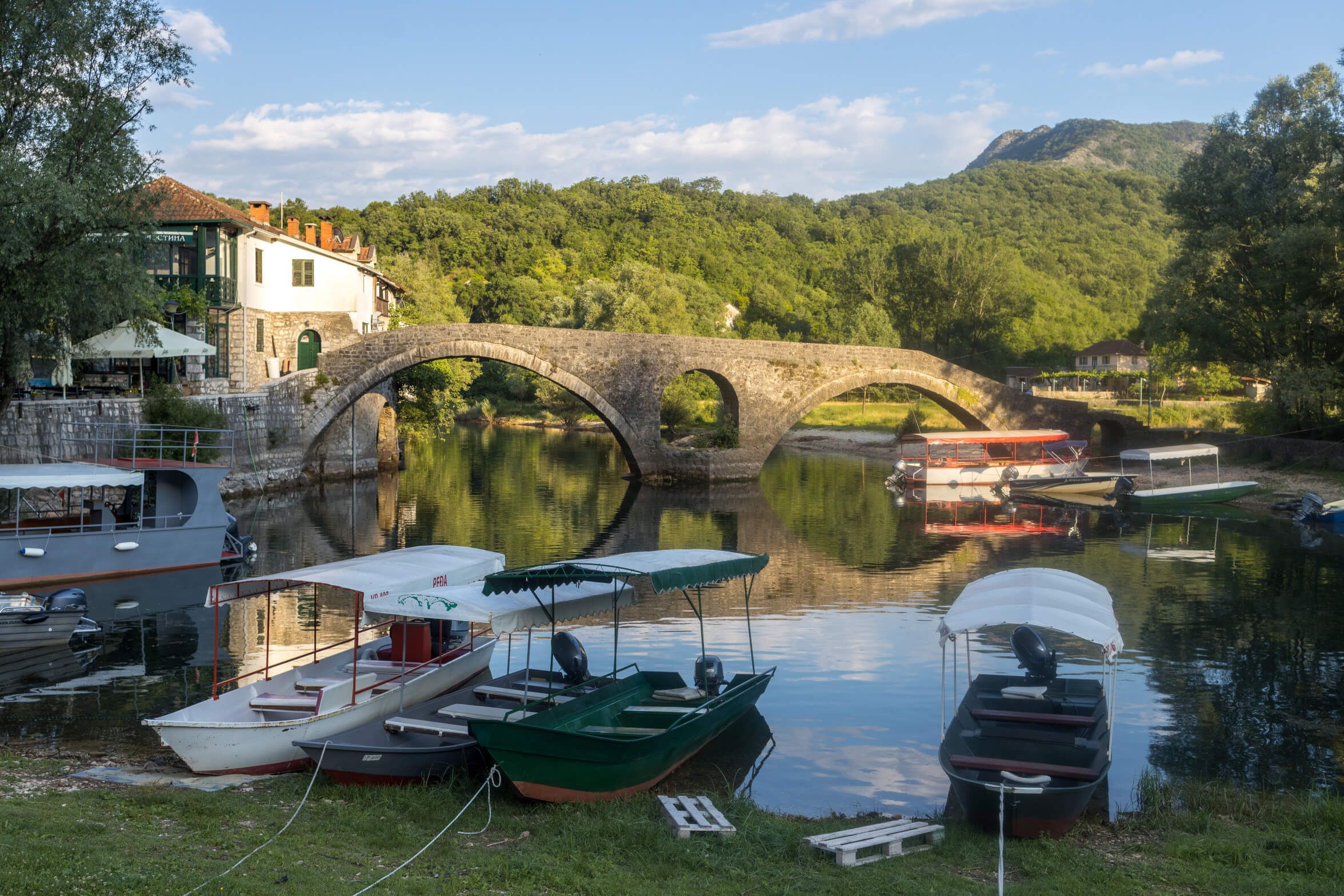 Eine ruhige Landschaft mit einem alten Steinbogen und Booten im Wasser, umgeben von der Natur.