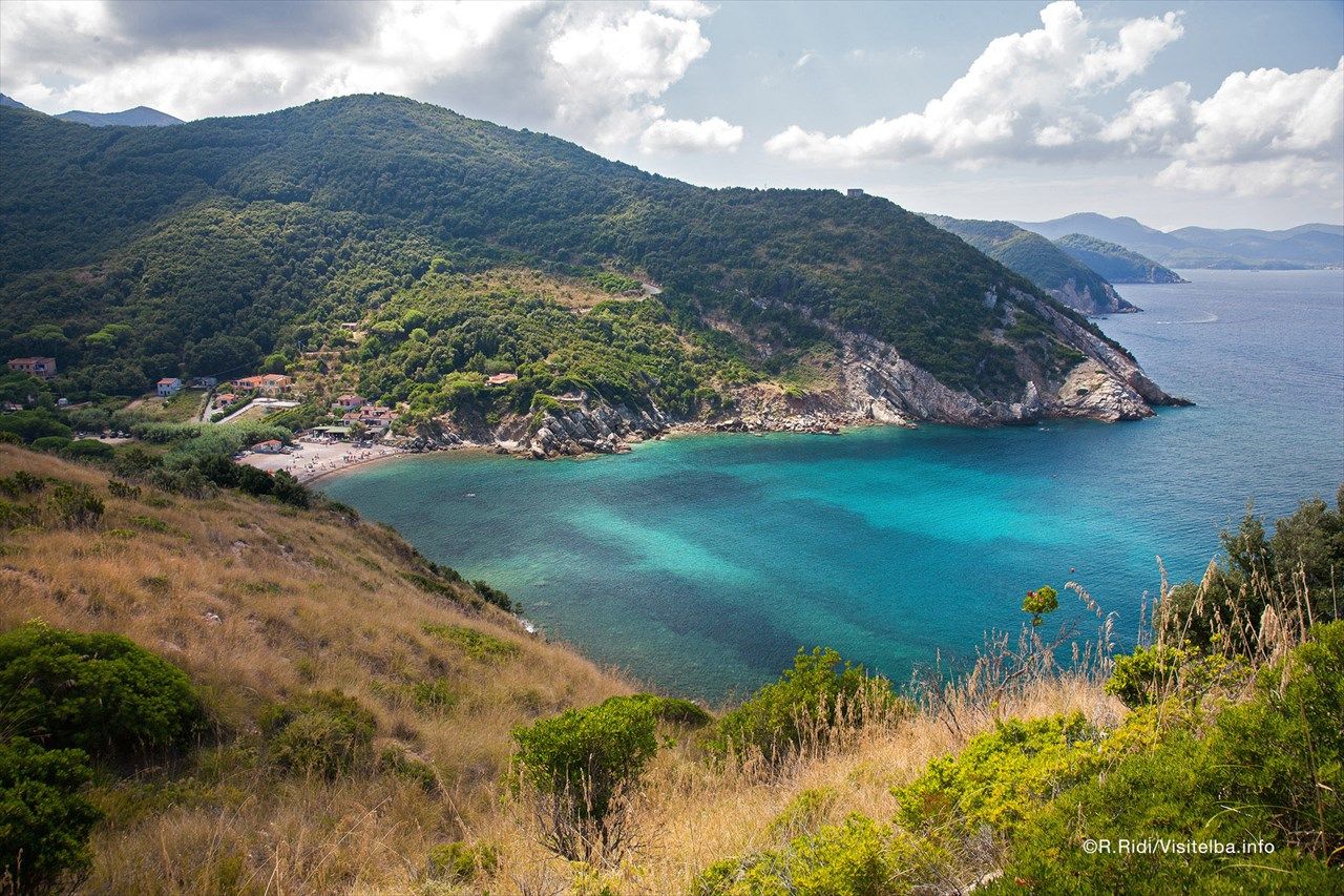 Ein malerischer Küstenblick mit türkisfarbenem Wasser und grünen Hügeln, darunter ein kleiner Strand.