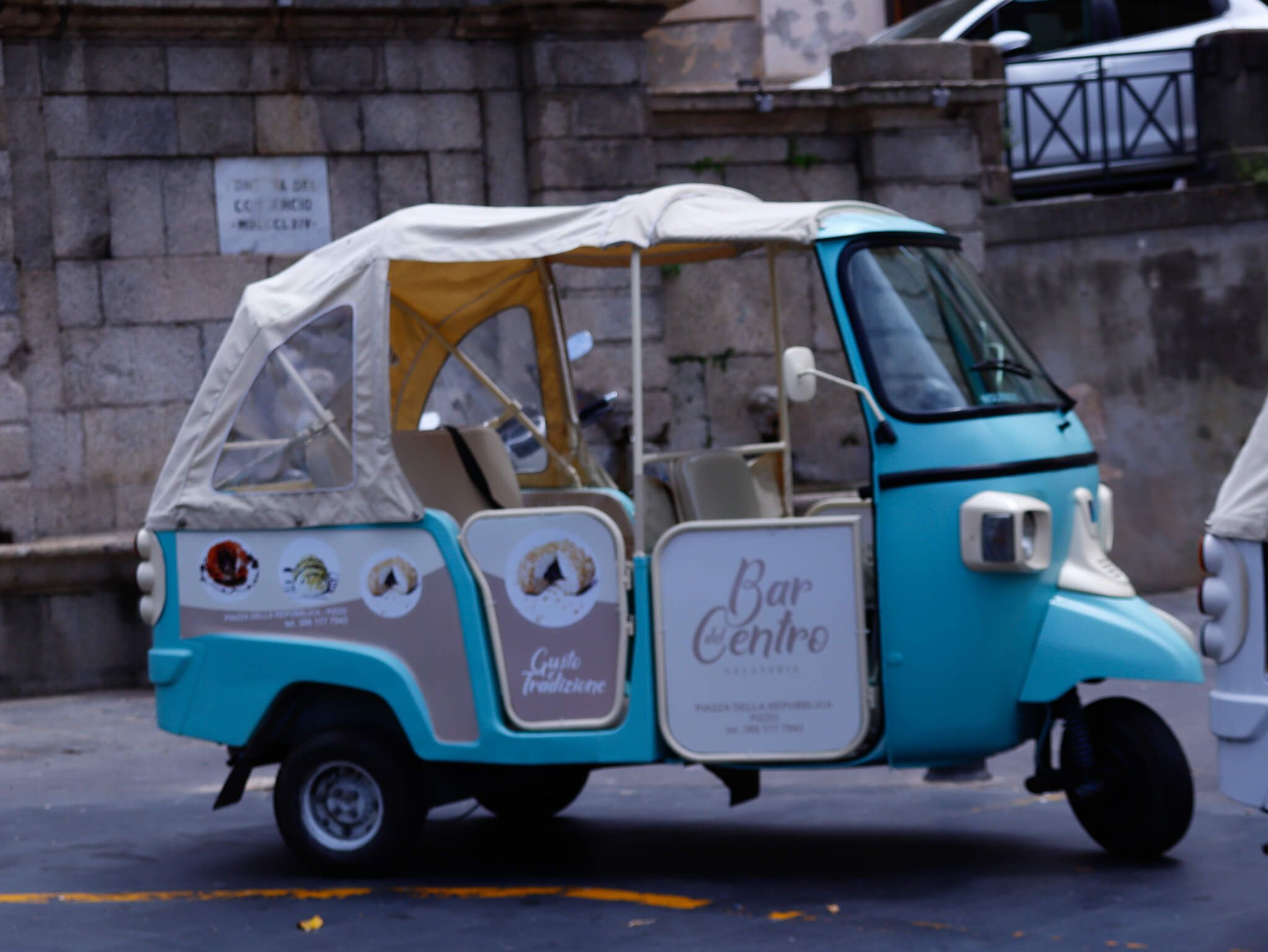 Ein niedlicher, türkisfarbener Tuk-Tuk mit einem hellen Dach, gekennzeichnet mit Bar Centro und verschiedenen Logos.