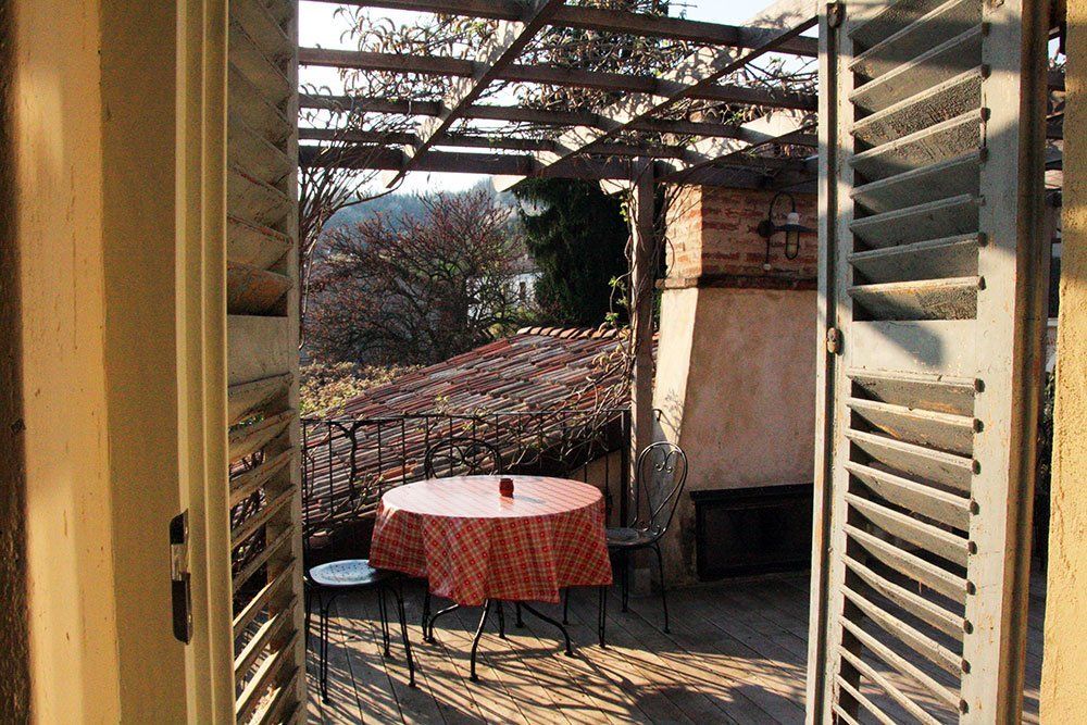 Ein Tisch mit kariertem Tuch und Stühlen auf einer Terrasse, umgeben von Pflanzen und einem schönen Ausblick.